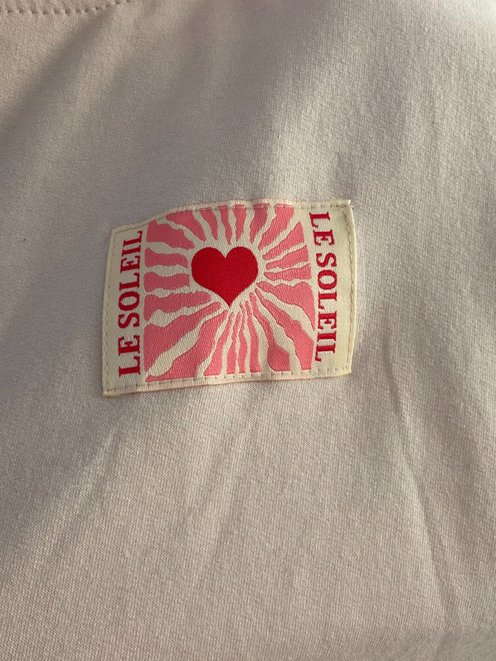 Detail des Le-Soleil-Herz-Patches auf dem beigen Langarmshirt