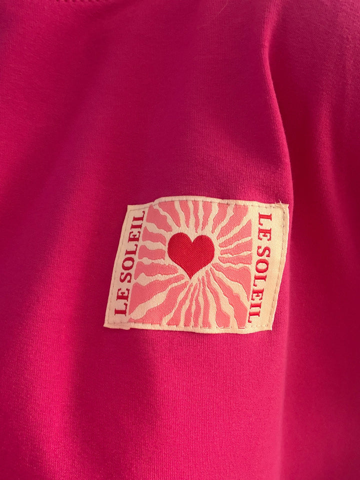 Detail des Le-Soleil-Herz-Patches auf dem pinken Langarmshirt
