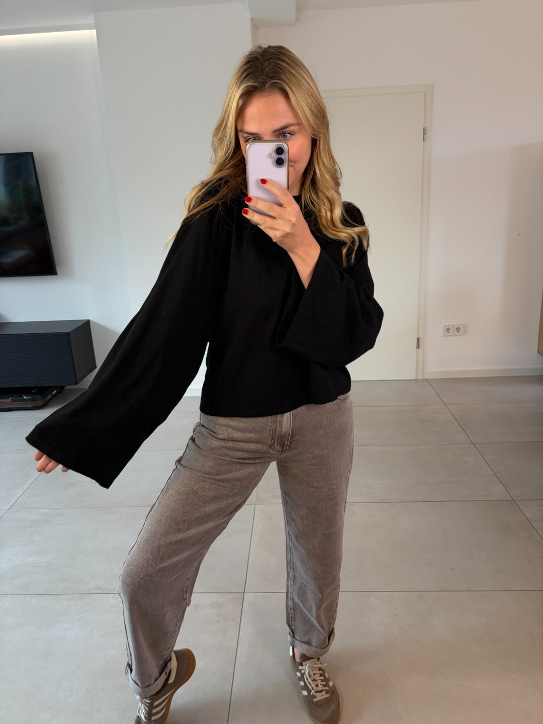 Oversize-Langarmshirt in Schwarz kombiniert mit graubrauner Jeans und Sneakern